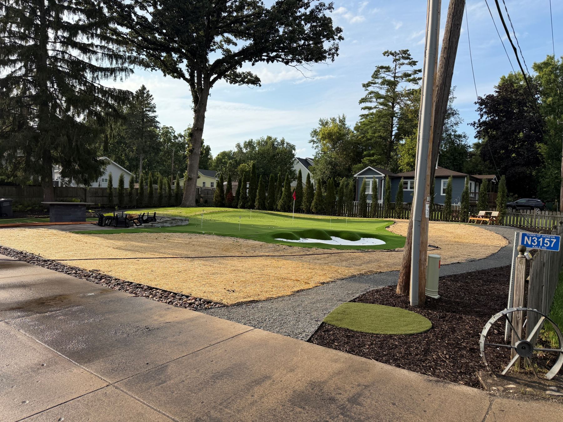 Backyard putting green with flag and bunker, fire-pit patio and arborvitae privacy screen